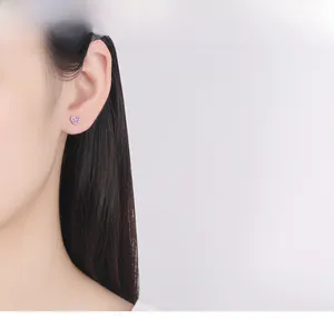 Close-up of heart-shaped silver stud earring featuring sparkling pink zircon on an earlobe
