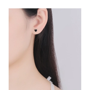 Close-up of minimalist black heart stud earring worn on ear with rose gold screw back