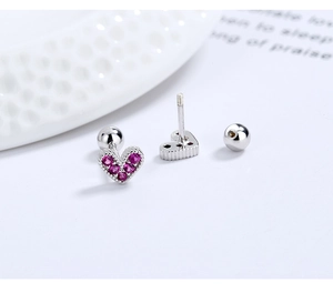 Macro view of heart-shaped S925 silver stud earrings with red zircons and screw backs