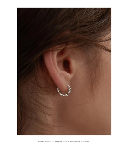 Detail of mirror silver Mobius hoop earring with twisted texture on model ear