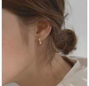 Close-up of a minimalist golden Mobius twist hoop earring worn on a model's ear