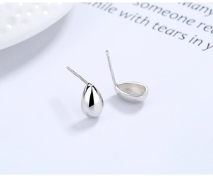 Macro view of polished S925 sterling silver teardrop studs on a minimalist white table
