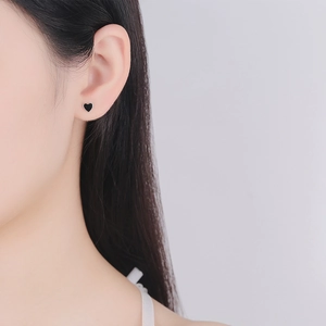 Minimalist black enamel heart stud earring in 925 sterling silver worn on earlobe