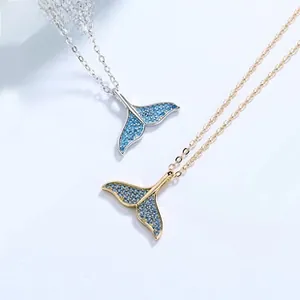 Close-up of gold and silver whale tail pendants with pavé blue zircons on fine chains