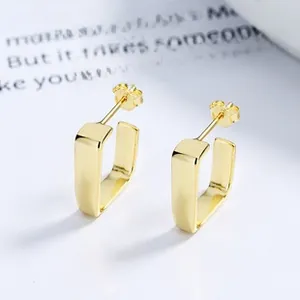 Detail view of golden U-shaped geometric earrings on a minimalist decorative background