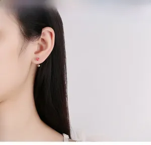 Close-up of red enamel heart earring with silver ball detail worn by a model