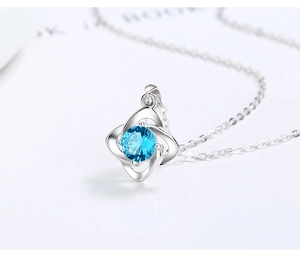 Detailed close-up of a silver four-leaf clover necklace with a sparkling blue zircon stone