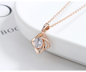 Macro shot of rose gold clover pendant with sparkling zircon on a white jewelry stand