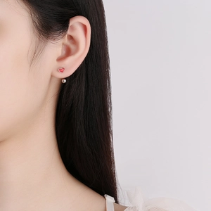 Minimalist red heart enamel earrings with silver beads worn by a female model