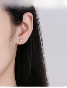 Close-up of geometric silver stud earring with iridescent moonstone on female ear