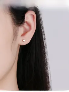 Close-up of minimalist silver cube stud earrings worn on the earlobe with a soft glow