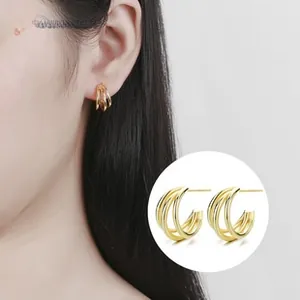 Close-up of triple-layered golden C-shaped stud earrings with a polished glossy finish