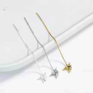 Detailed view of origami bird tassel earrings in gold and silver hanging on white
