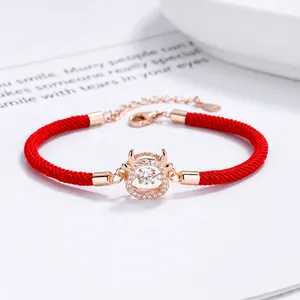Detalle de pulsera tejida roja con dije de buey en oro rosa y circonitas incrustadas