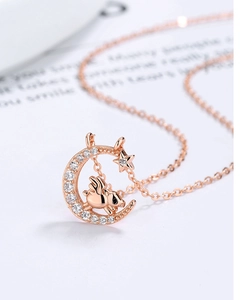 Vista macro de collar de oro rosa con una luna creciente con circonitas y cerdo alado
