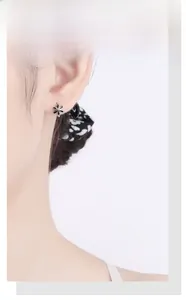 Gros plan d'une boucle d'oreille fleur noire avec bords argentés portée par un mannequin