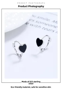 Détail de boucles d'oreilles en argent 925 avec pendentif cœur noir sur texture blanche