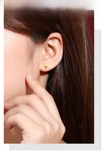 Close-up of golden matte round ball stud earring worn by a model in a natural setting