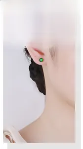 Close-up of emerald green zircon stud earrings on model's ear featuring four-prong gold setting