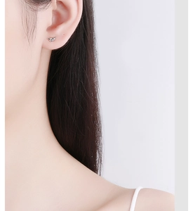 Close-up of a minimalist silver knot stud earring worn on the earlobe with a white background