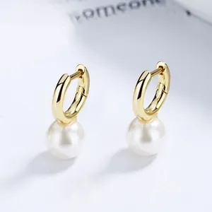 Detailed close-up of gold hoop earrings with white freshwater pearl drops on white base