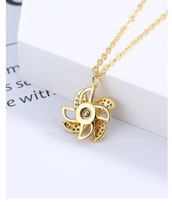Close-up of a golden spinning windmill pendant necklace with zircon inlay on a white stand