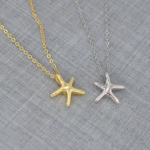 Detailed view of polished starfish pendants in gold and silver on textured fabric