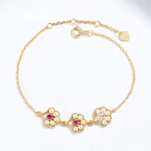 Close-up of gold bracelet with ruby floral pendants surrounded by small white pearls