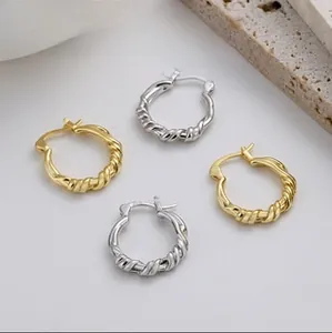 Detailed view of twisted rope texture earrings in gold and silver on a minimalist setup