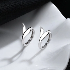 Macro detail of silver fishtail hoop earrings on a textured ceramic tray with elegant lighting