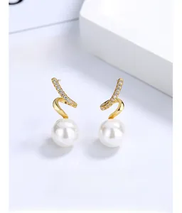 Close-up of golden spiral wave earrings with white pearl and sparkling rhinestones