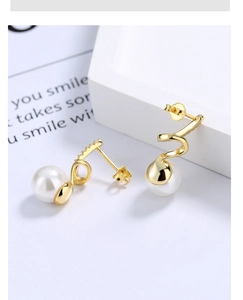Macro shot of wavy gold spiral earrings with tiny diamonds and round white pearl