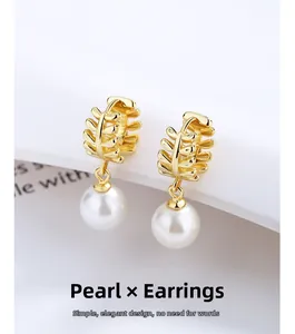 Detail of gold leaf stud earrings featuring a lustrous round white shell pearl dangle