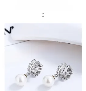 Macro shot of silver leaf-shaped earrings with white pearls on a minimalist background