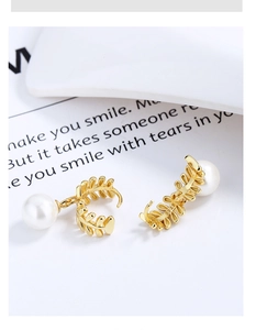 Macro shot of S925 leaf earrings featuring detailed golden feathers and white pearls