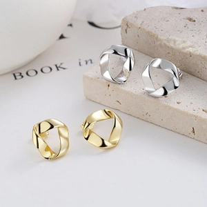 Close-up of gold and silver twisted geometric drop earrings on minimalist stone props