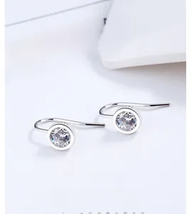 Detail of silver drop earrings featuring bezel-set round cubic zirconia on long hooks