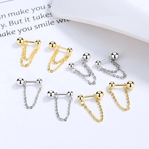 Dettaglio di orecchini a catena minimalisti in oro e argento su sfondo bianco