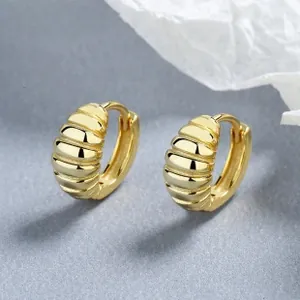 Détail de créoles dorées style croissant avec une texture métallique nervurée