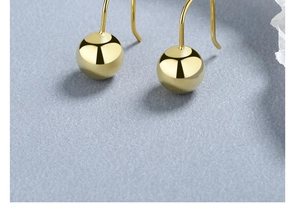 Detailed close-up of polished golden sphere earrings with classic hook on a blue surface