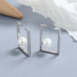 Detailed close-up of rectangular silver earrings with lustrous white pearls on a soft background