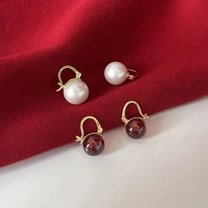 Dettaglio di eleganti orecchini a goccia con perle bianche e rosse e ganci dorati su tessuto