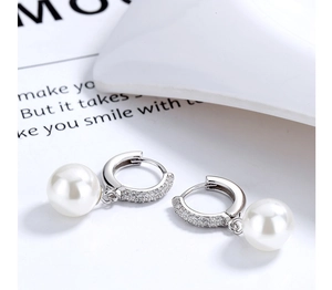 Close-up of elegant pearl drop earrings with crystal pavé hoops on a magazine background