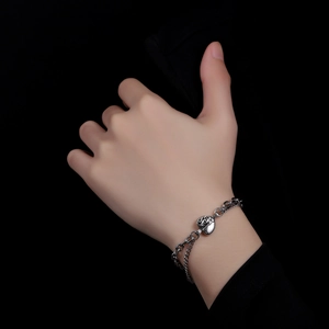 Close-up of a silver double-chain bracelet with a heart pendant featuring a tree design