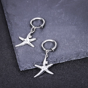 Détail de boucles d'oreilles étoile de mer argentées avec perle sur fond pierre