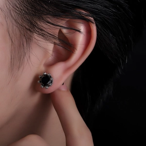 Close-up of black zircon stud earring with silver crown setting on a male model's ear