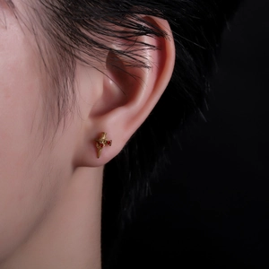 Close-up of golden sword stud earring with red gemstone on model with dark background