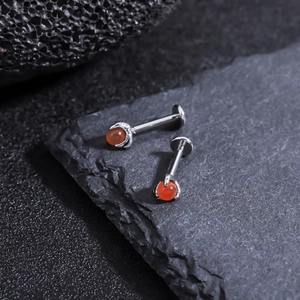 Macro shot of silver titanium dragon claw stud with red zircon on black rock surface