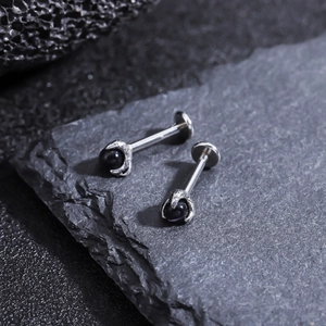 Detailed view of silver dragon claw stud earrings with black zircon on dark rock