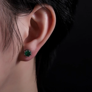 Green zircon crown stud earring with silver metal claws on a black background